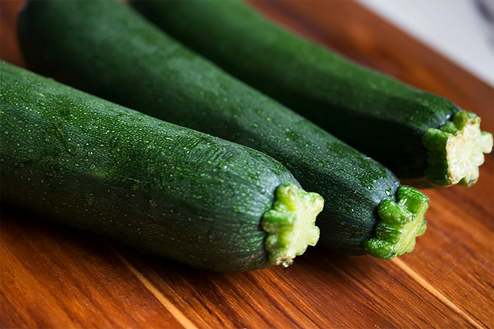 Close-up of three fresh green zucchinis on a wooden surface, perfect for food themes.