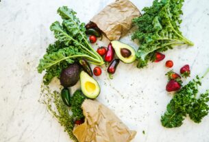 Avocado, kale, and more fresh produce artfully arranged on a marble surface.